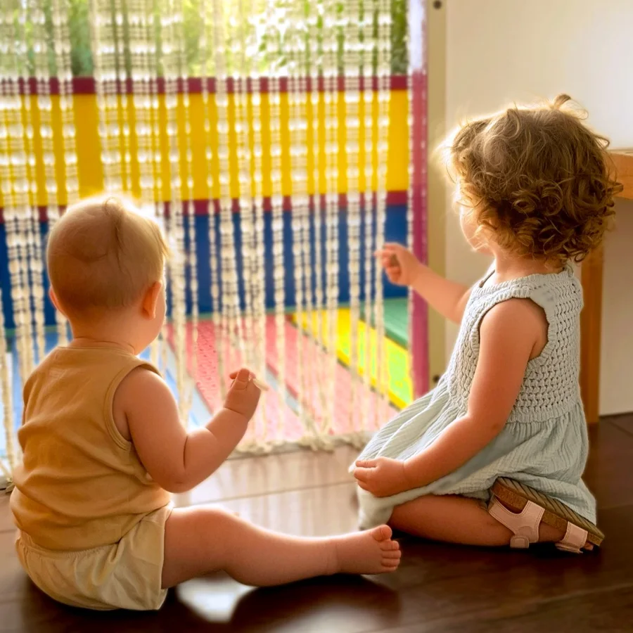 Two young children sitting by a colourful bead curtain